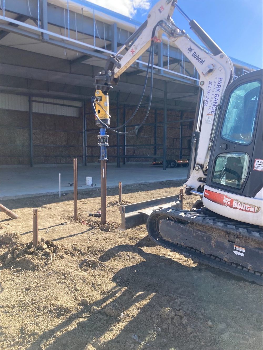 Park Range excavator installing helical piles beside a hangar at Aero FNL, Loveland