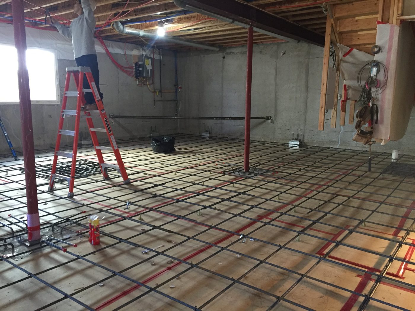 Rebar grid tied in place over forms for a new structural floor in a home basement, with temporary shoring posts