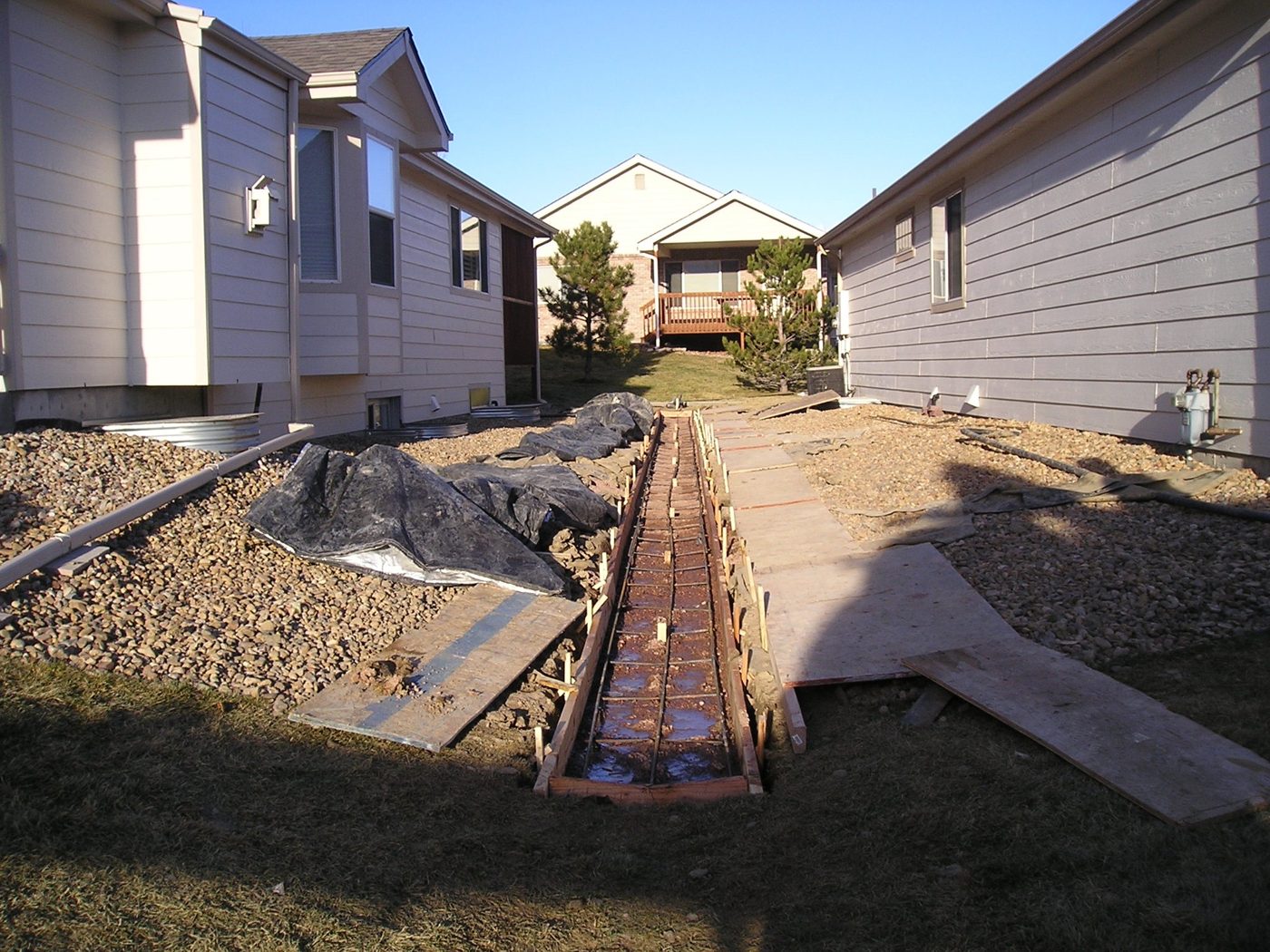 Formed and reinforced concrete drainage pan between two homes, with the regraded swale alongside