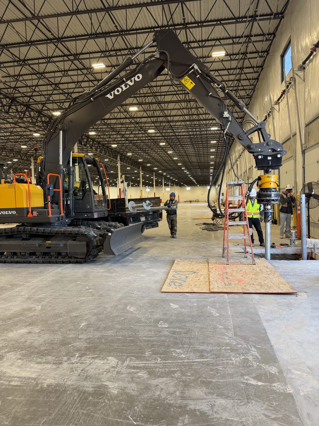 Park Range crew installing helical piles with an excavator inside the warehouse for the Falcon Crane project