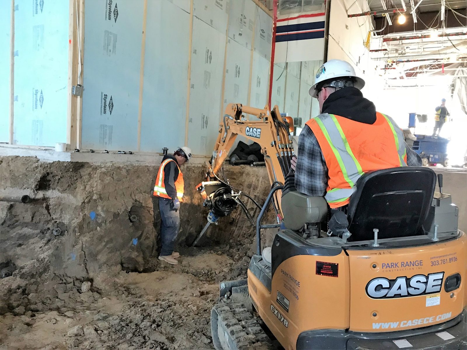 Park Range crew drilling with a compact excavator in an excavation inside an existing building