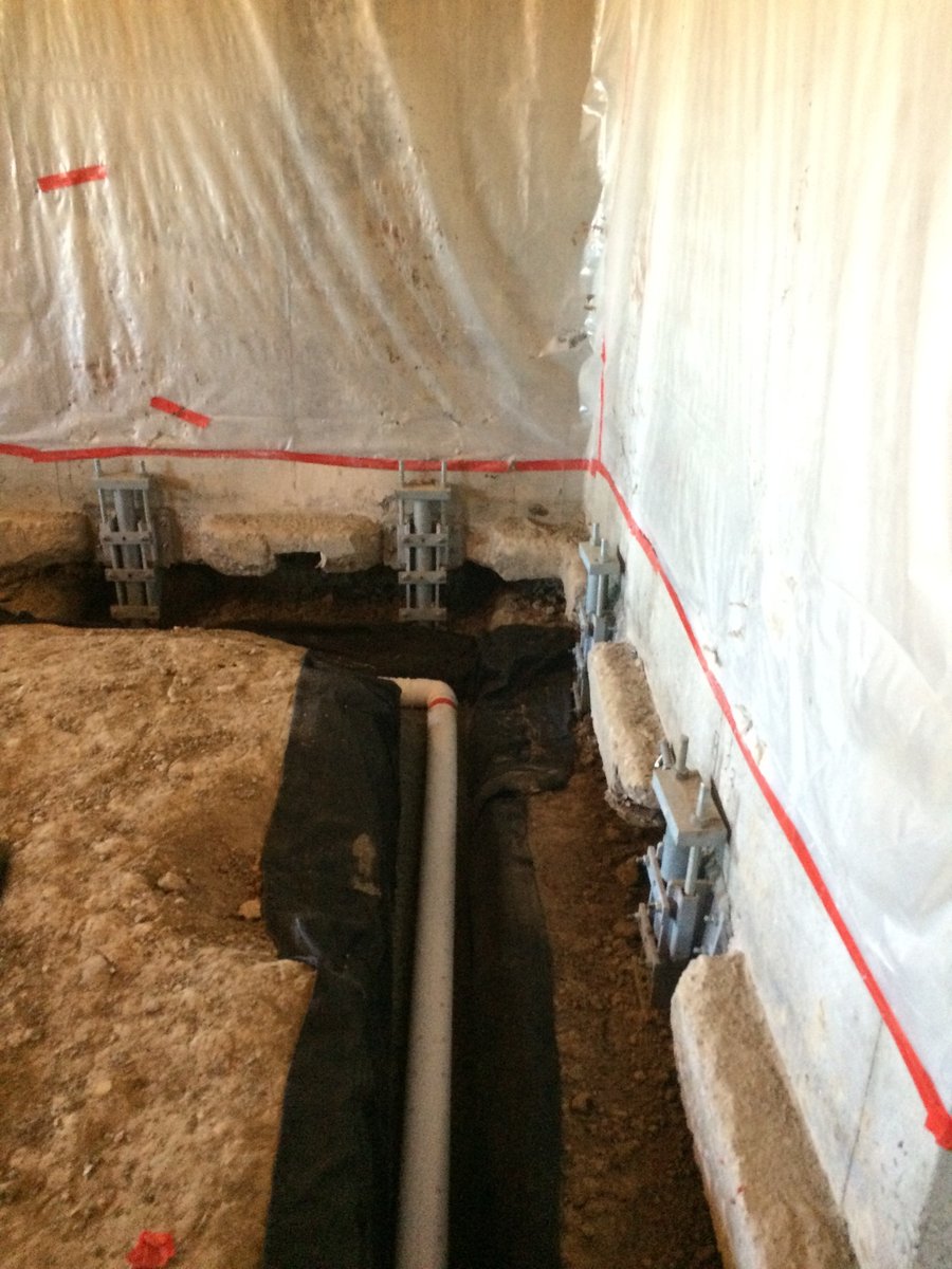 Interior perimeter drain pipe in a trench along an underpinned basement foundation wall