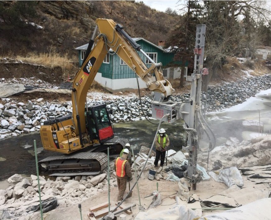 Park Range crew drilling cased micropiles with an excavator-mounted TEI drill beside the creek for the new Lyons bridge abutments