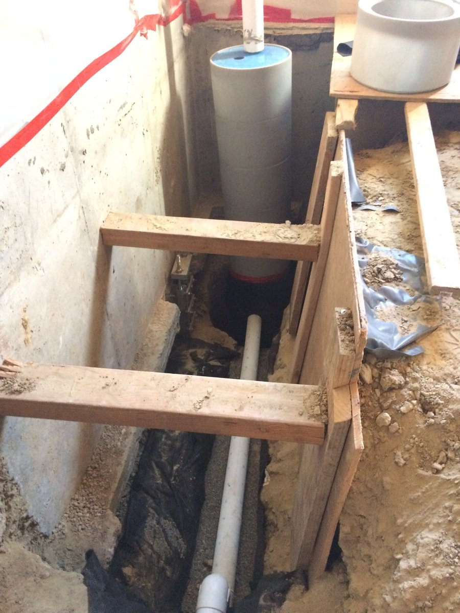 Interior drain pipe running to a new sump pit inside a shored trench